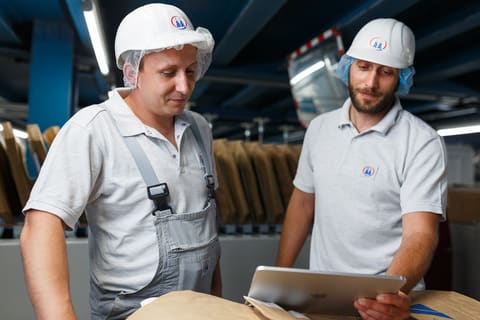 Deux techniciens casqués consultant une tablette dans un atelier